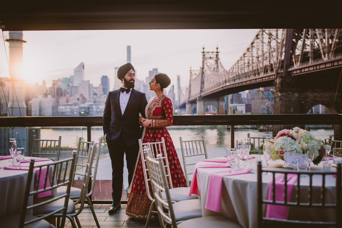 Sikh bride and groom look at each other in their wedding reception banquet hall at penthouse 808 with the queensboro 59th st bridge in the background