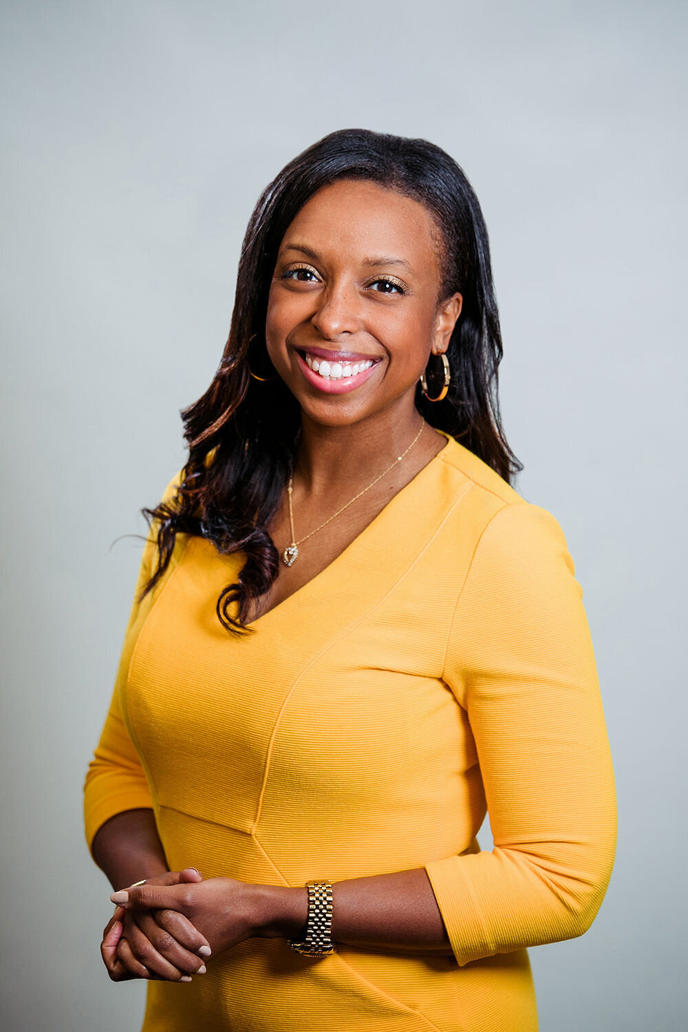A woman holds her hands together while wearing a yellow shirt.