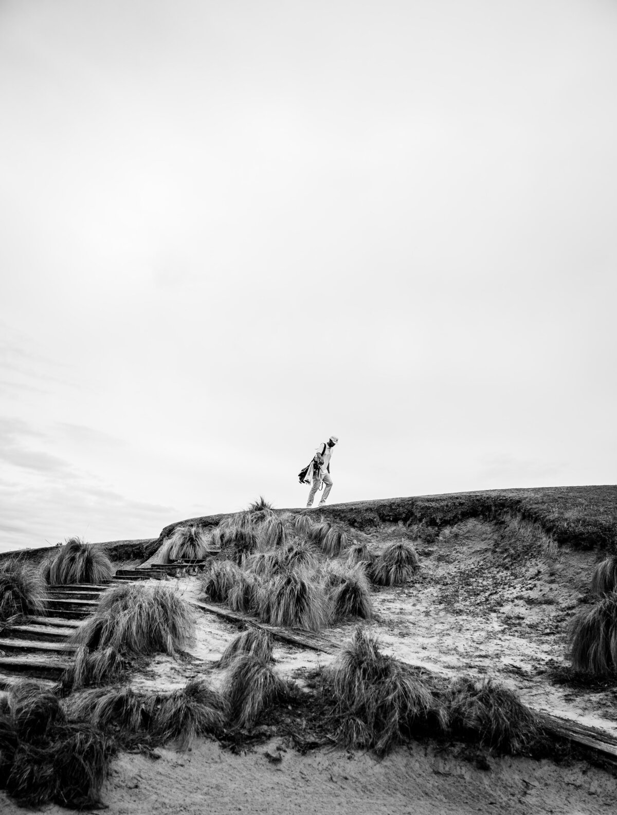 Dramatic Black and White image of golfer Matt Cardis walking above sand trap at Tobacco Road Golf Course in Sanford, NC in March 2020.