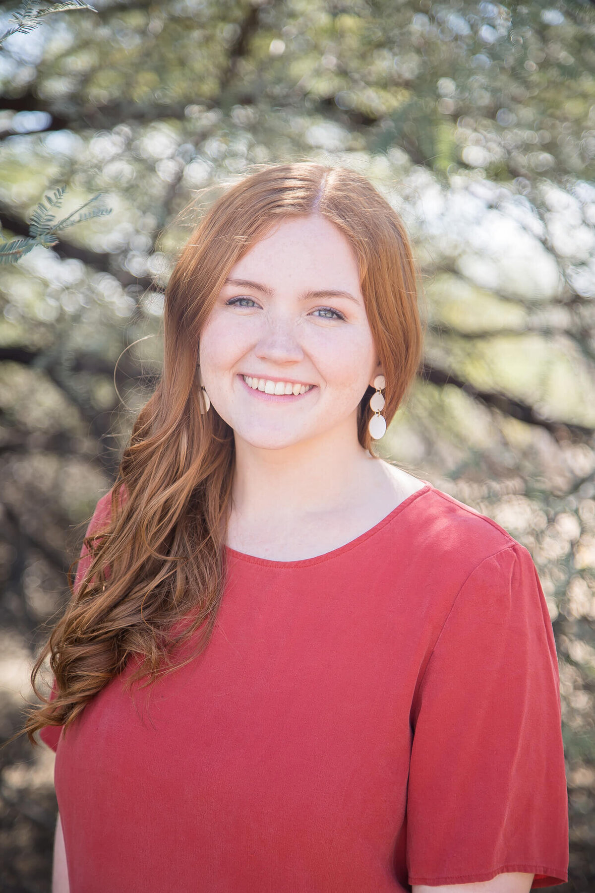 redheaded, blue eyed woman smiling in a desert park wearing a red shirt