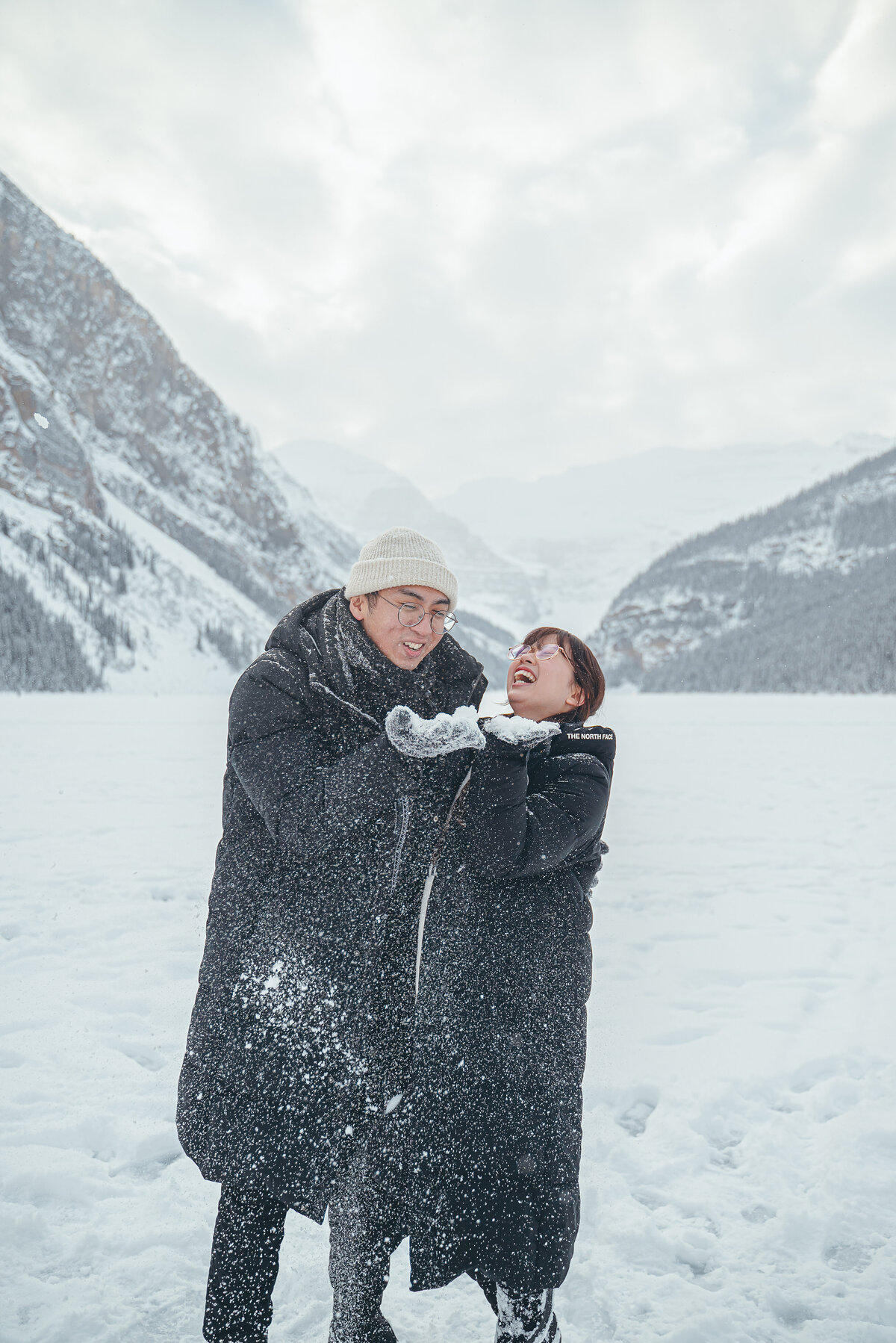 Playful couple throwing snow during Lake Louise photo session.