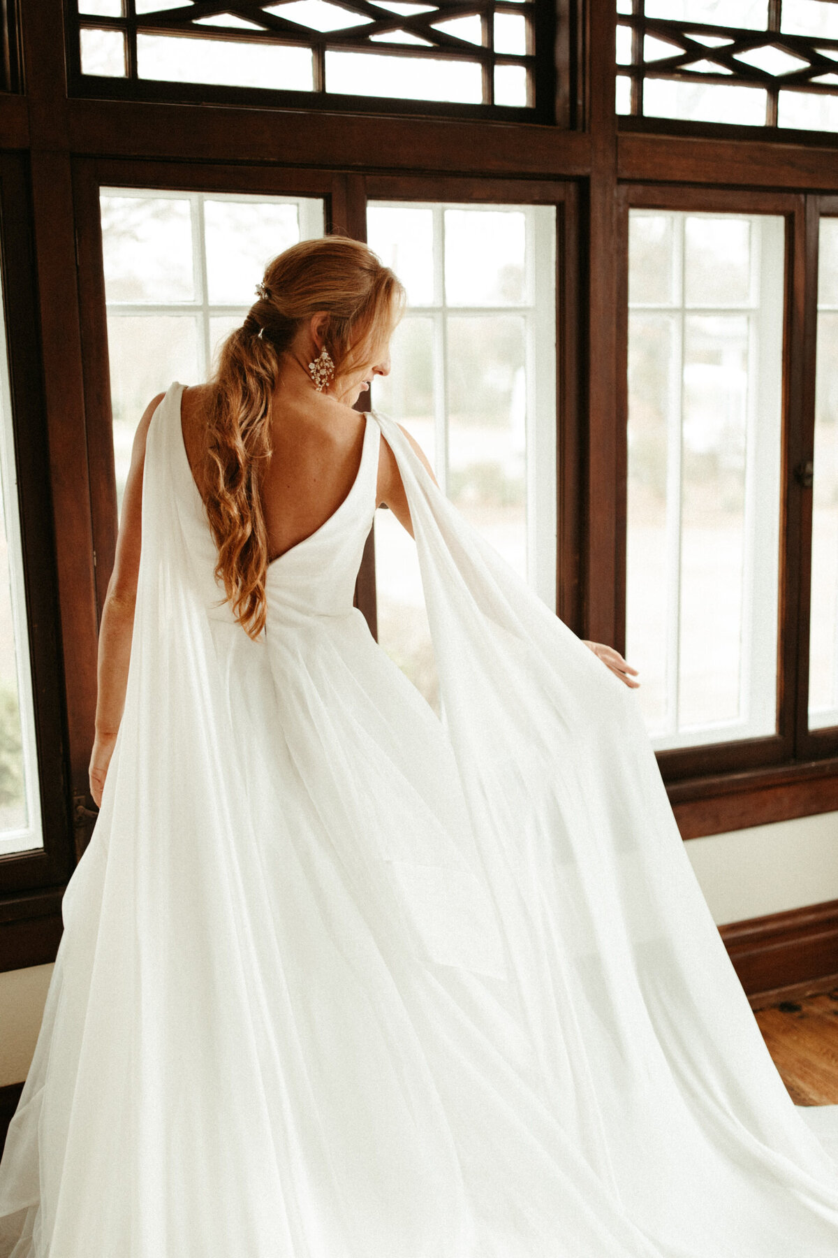 Bride with ponytail hairstyle waving her shoulder capes on her wedding dress