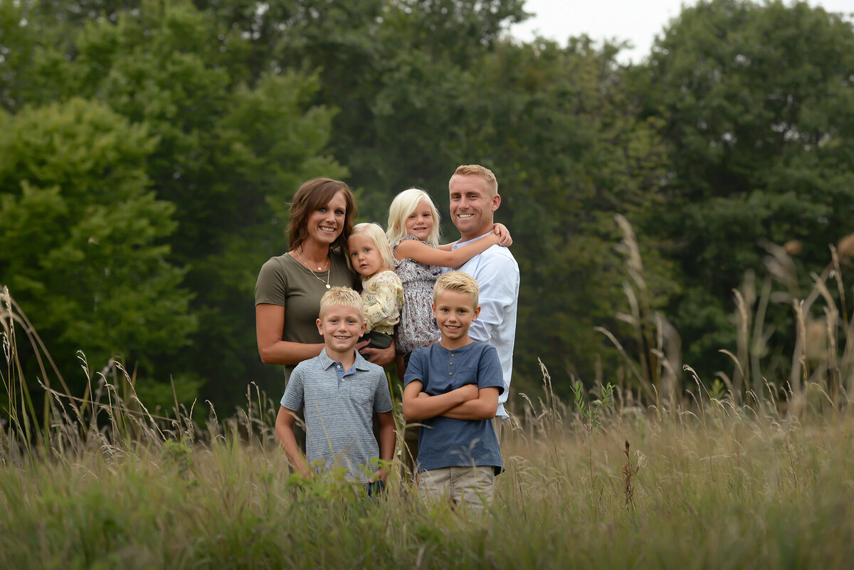 A family of 6 hug each other while they stand in tall grass