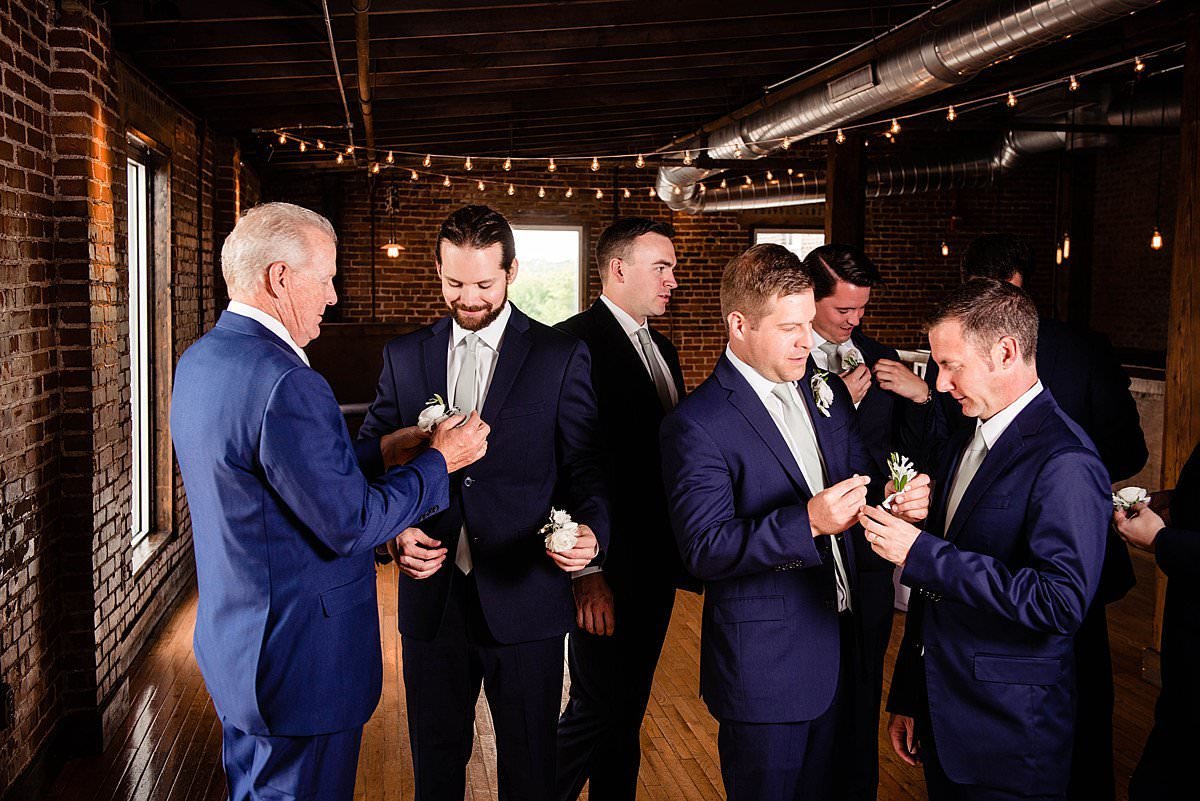 Gentlemen putting on boutonnieres, ivory roses on blue suits