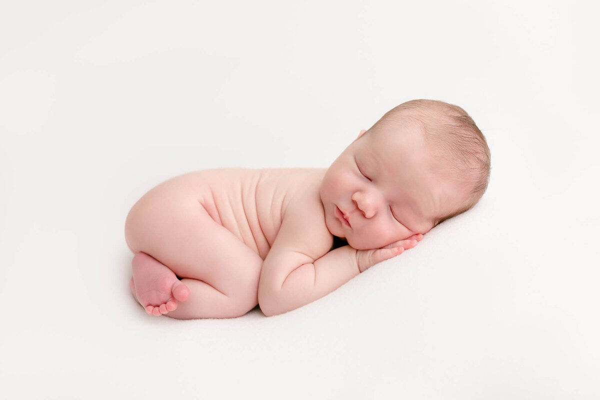 Newborn baby sleeping on belly with hand up by face on a white backdrop. Newborn photos with Ashlie Behm Photography
