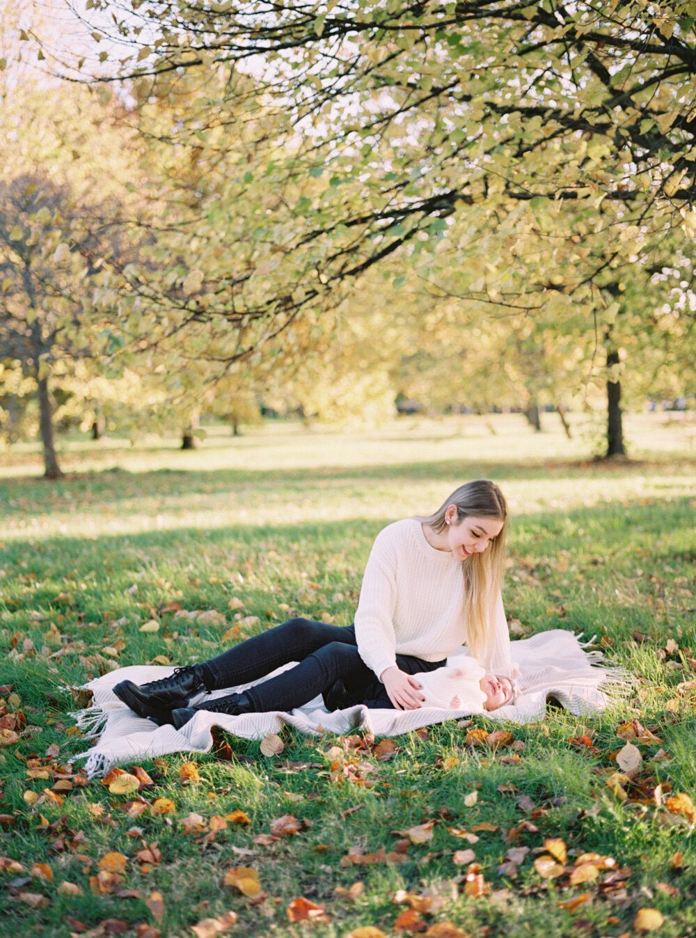 young mum with baby girl sitting on the blanket at park during autumn family photo session