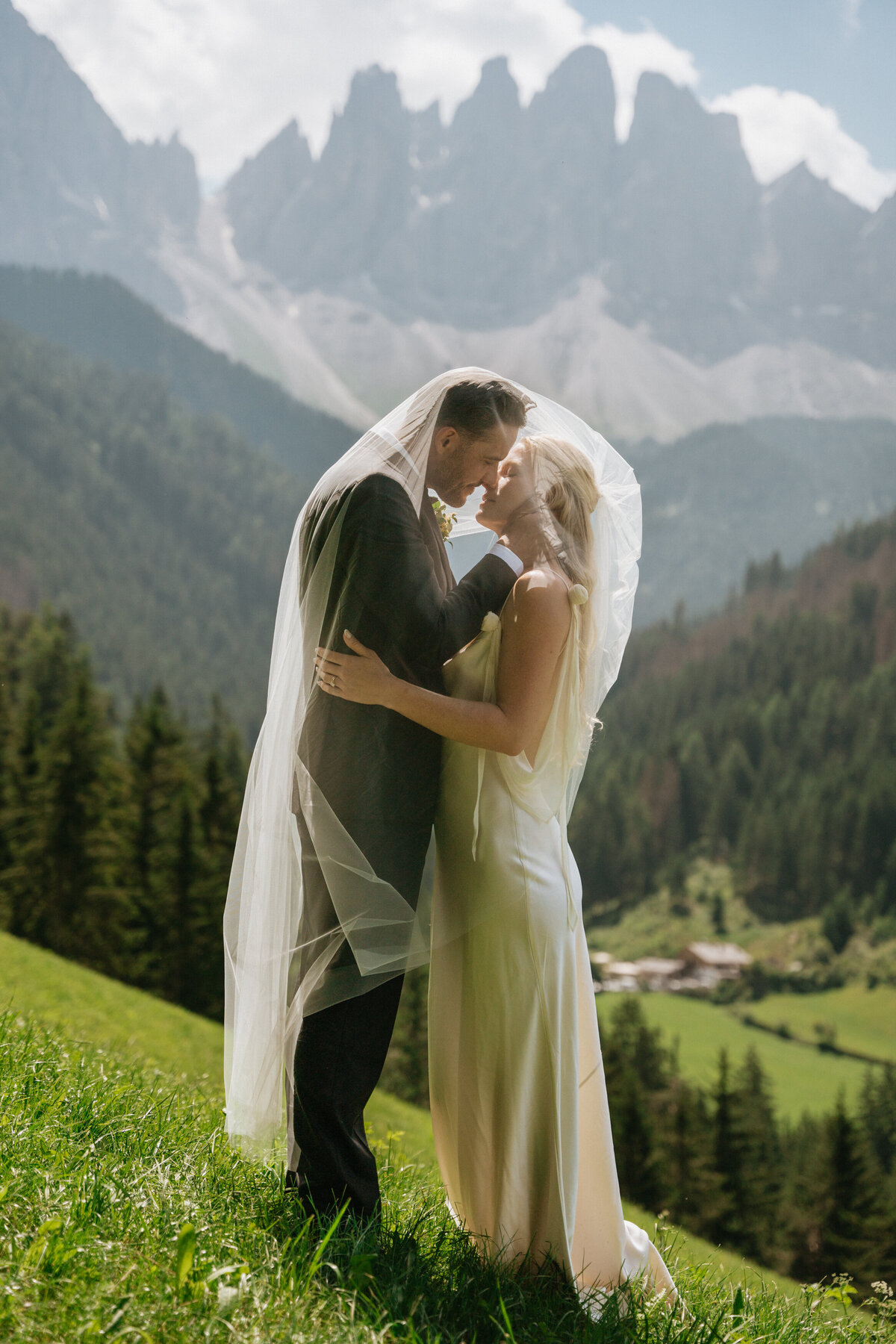 Bride and groom embracing with veil flowing in mountain meadow