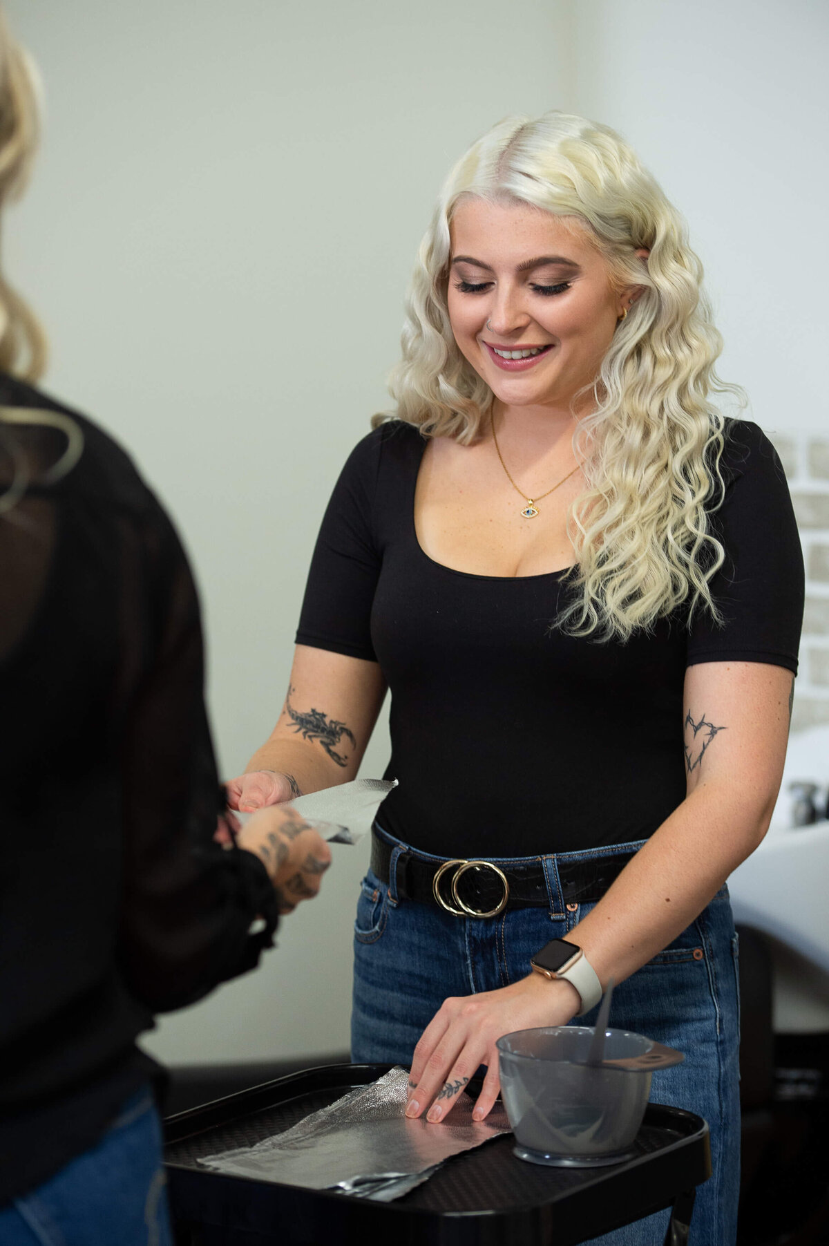 a blonde hair assistant in a black top passes foiling paper to a stylist.  Captured on-location at Richardson Hair Design by Ottawa branding photographer JEMMAN Photography