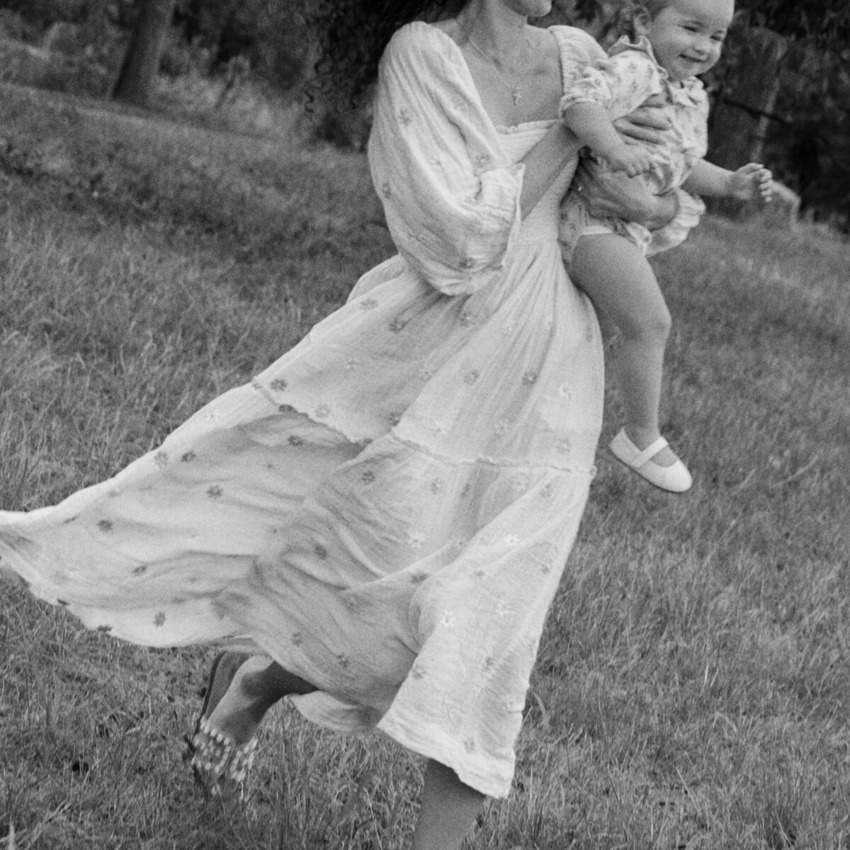 Black and white photo of mom in a long dress running while holding her baby