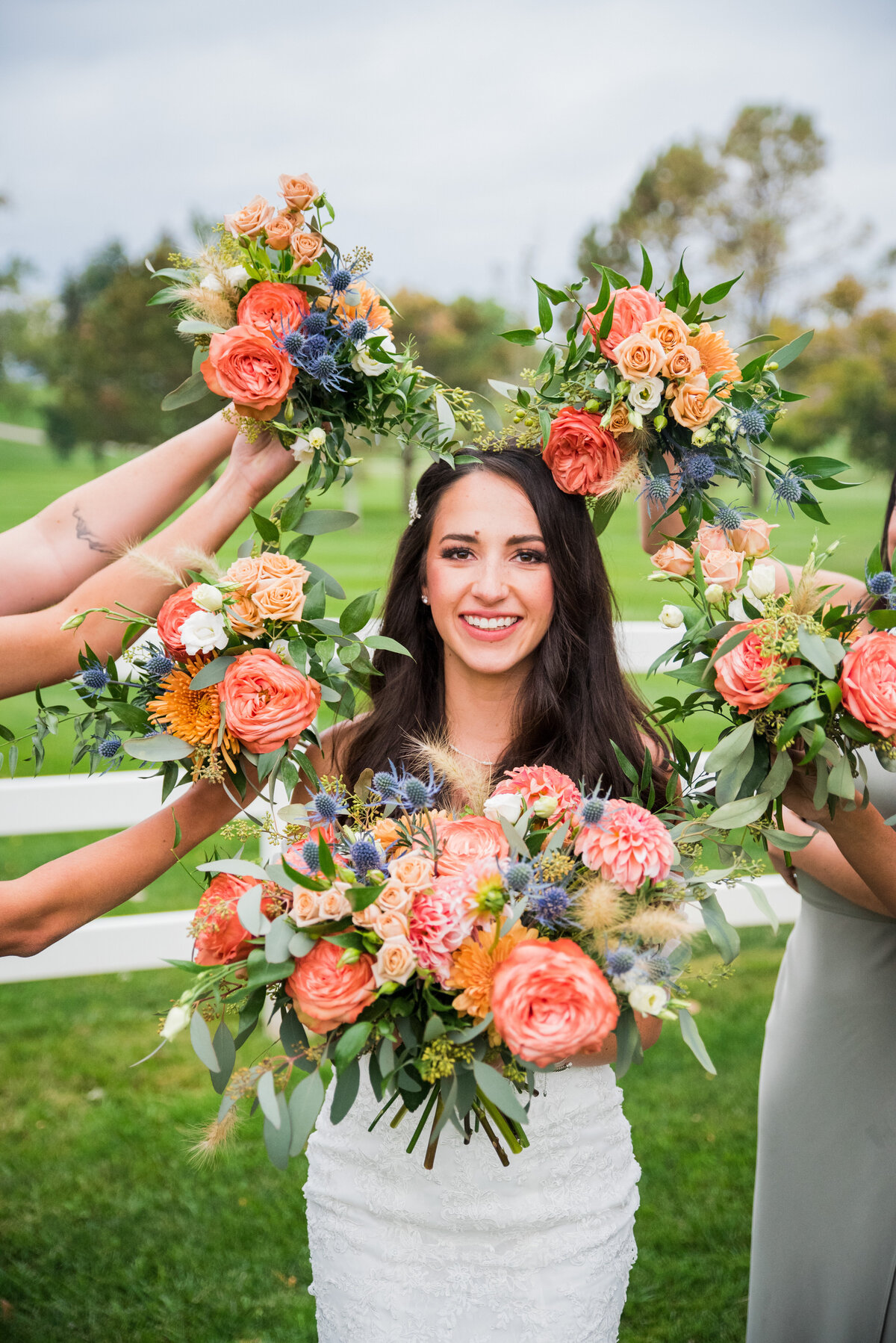A bride smiles at the camera with her bridesmaids bouquets framing her face.