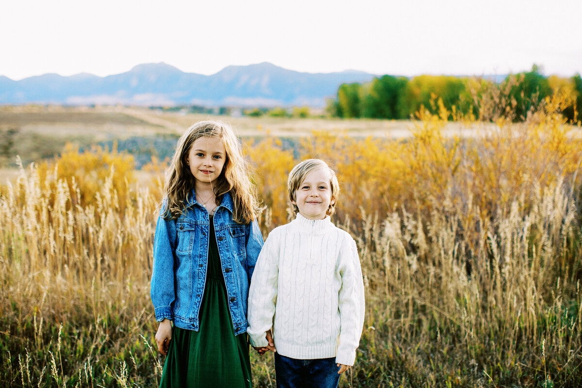 siblings stand in front of colorado mountains
