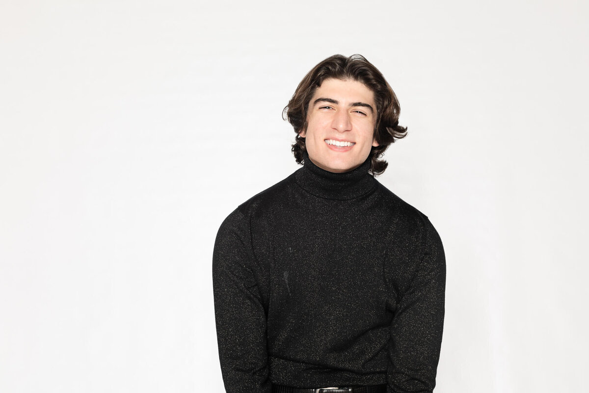 A person with shoulder-length dark hair, wearing a black turtleneck, smiles against a plain white background.