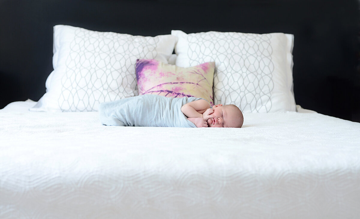 Infant boy laying on the master bed with white bedding.