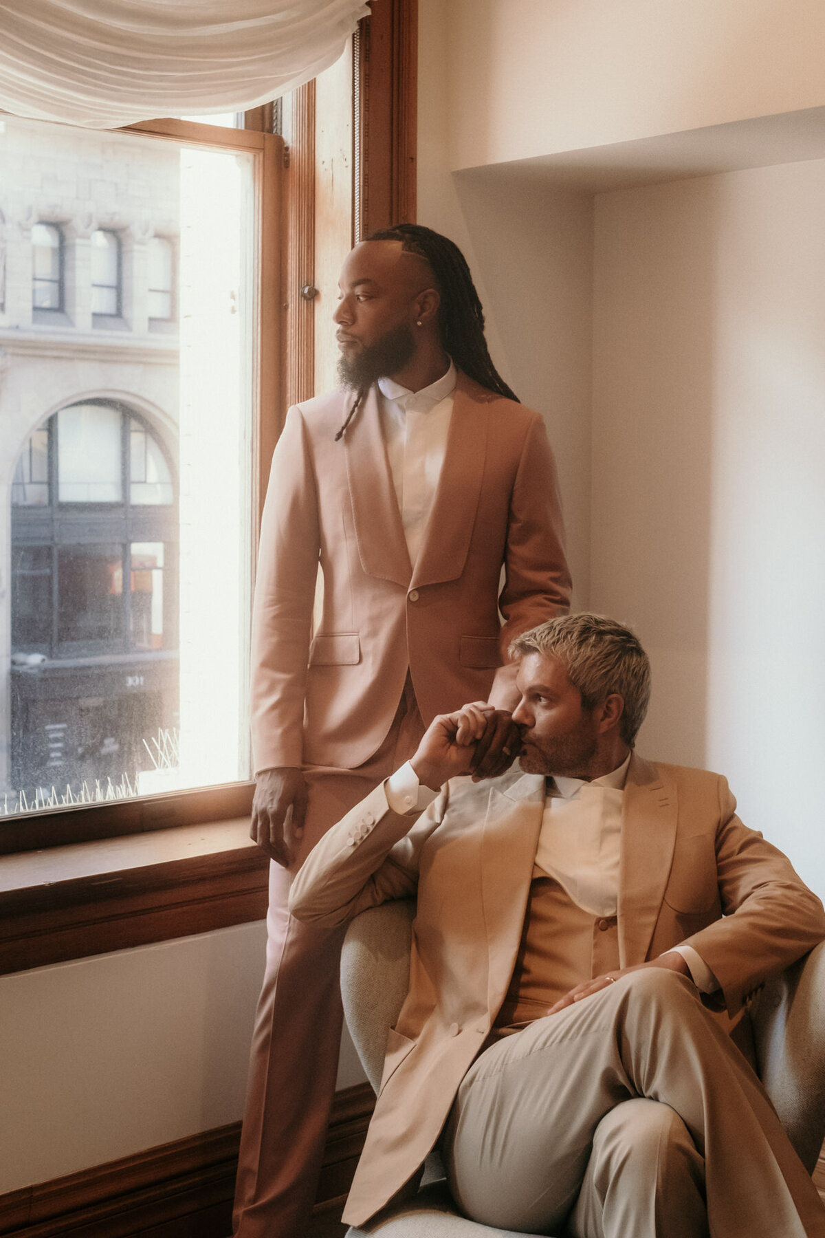 Couple photography in warm sunlight beside a window - both looking out.