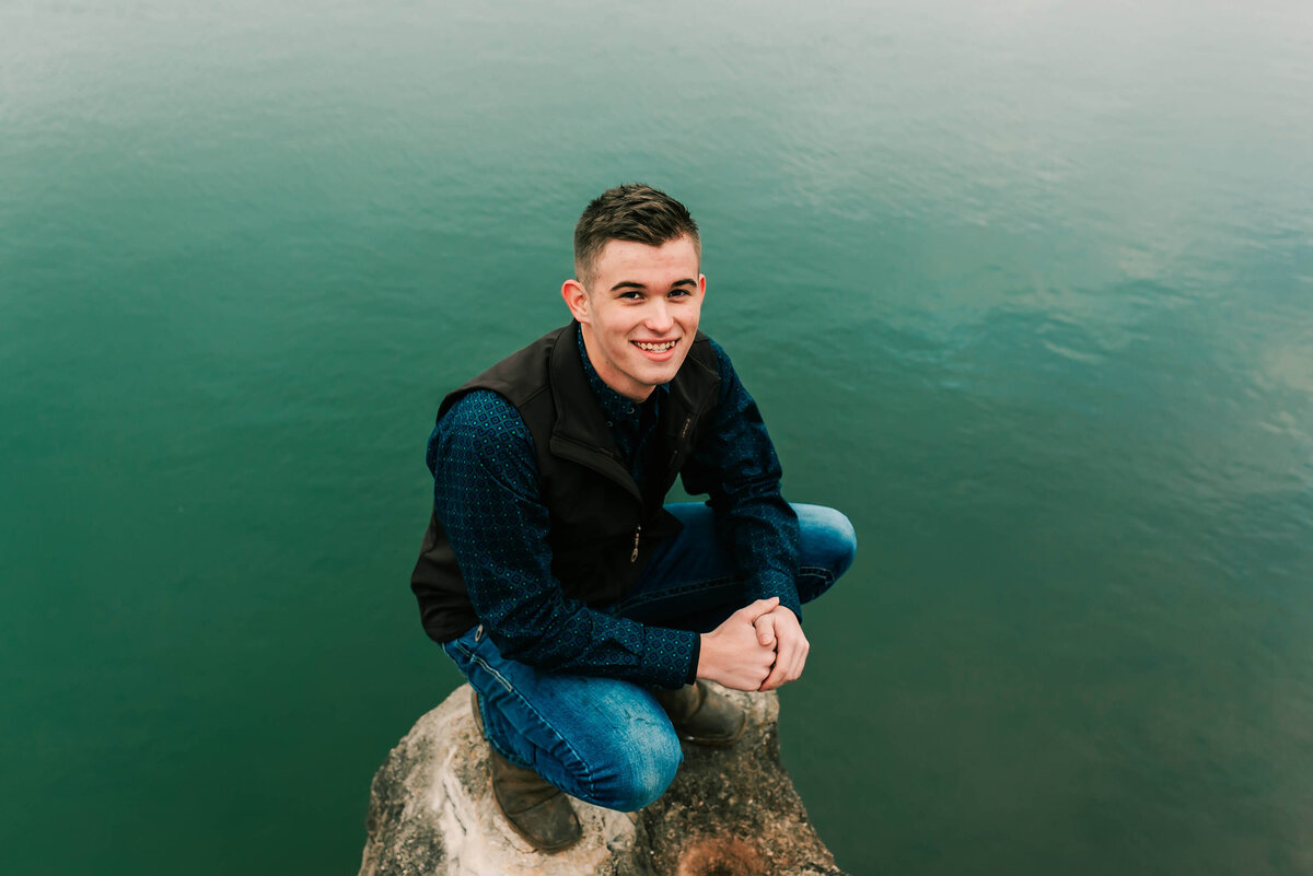senior boy squatting near a pond during Branson Missouri senior photographer