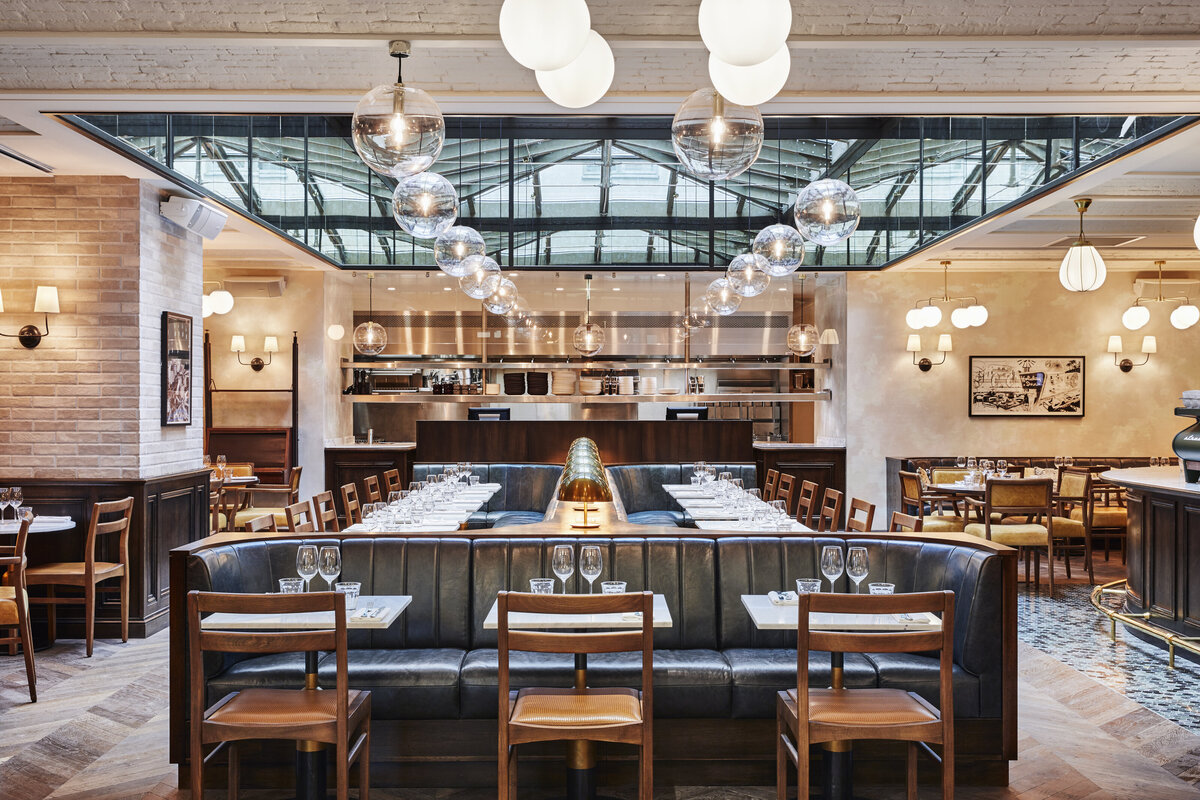 Restaurant with bancquettes featuring channel tufted leather upholstery, marble dining tables and wooden dining chairs with leather seats, and glass pendant lights