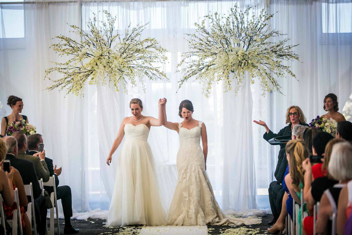two brides just married under white wedding arch