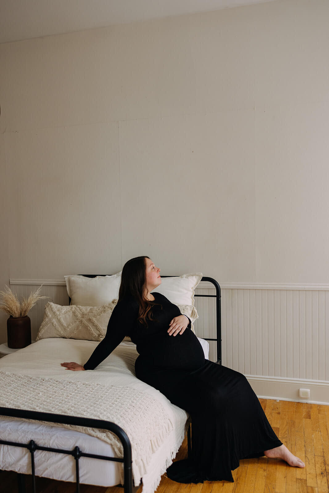 Woman sitting on bed with arm on baaby bump at  Finger Lakes Maternity session