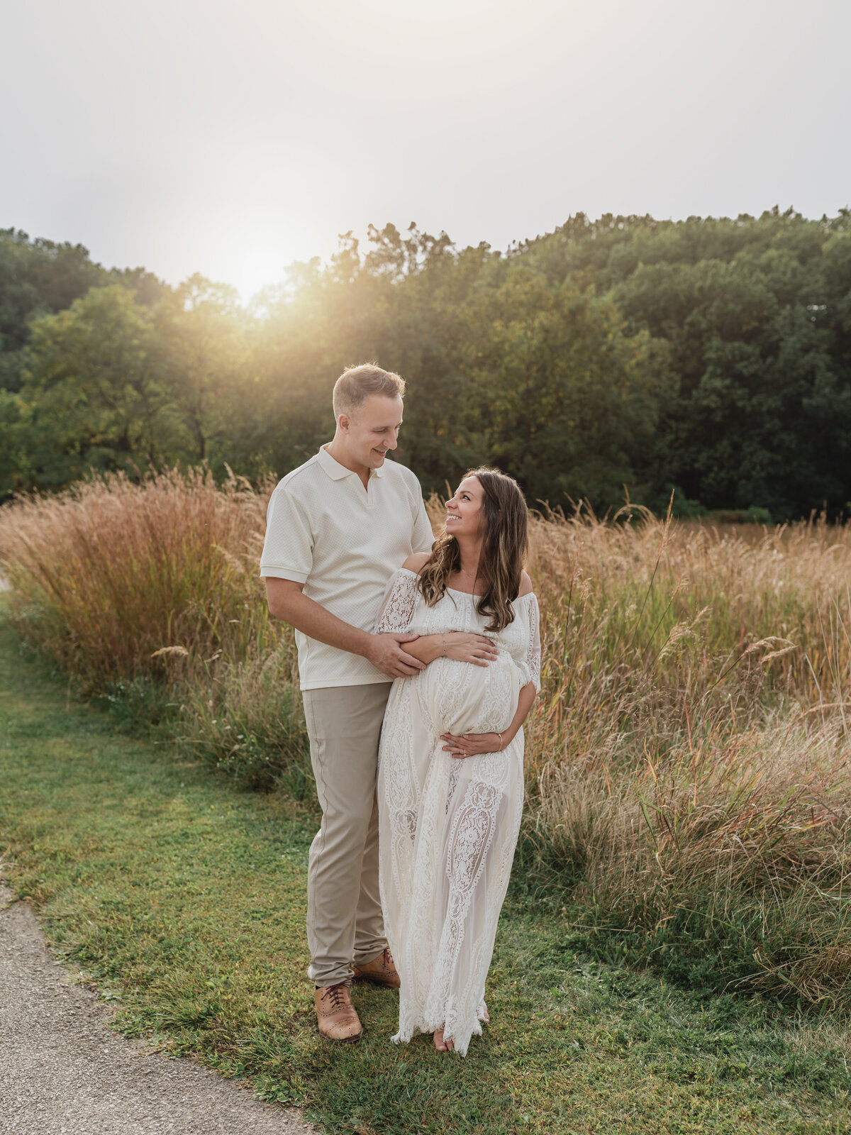 husband and pregnant wife in white lace maternity gown holding baby bump for maternity photoshoot