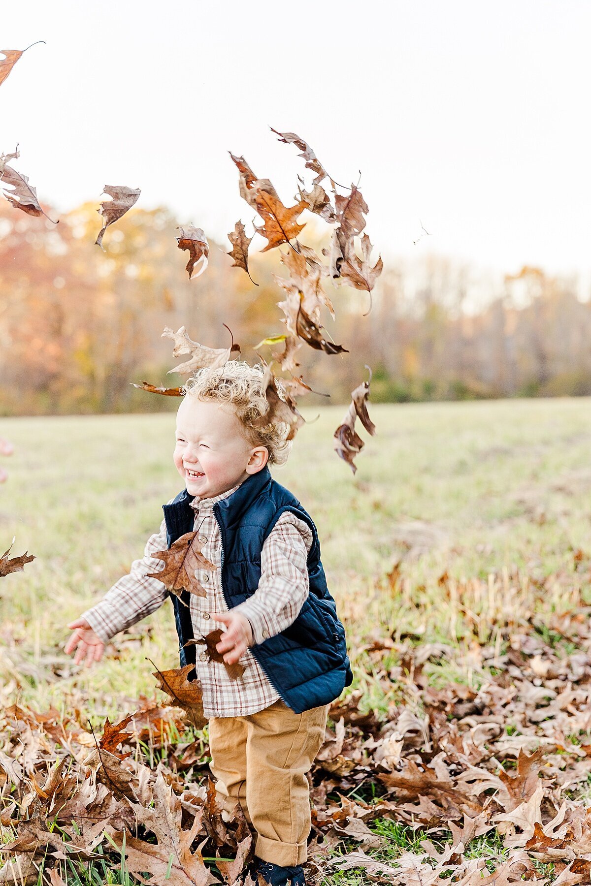 boy throws leaves  during winter maternity photo session with Sara Sniderman Photography at Heard Farm in Wayland Massachusetts