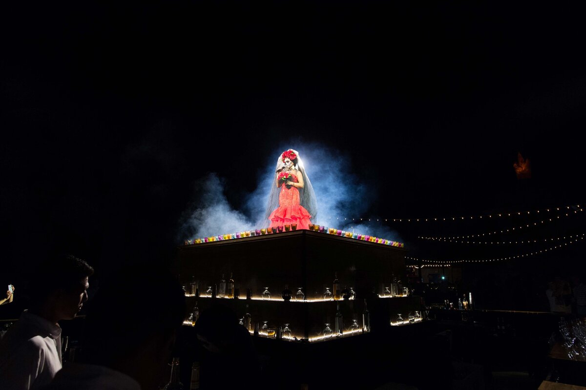 A women sings atop an outdoor bar while backlit by a spotlight as fog surrounds her