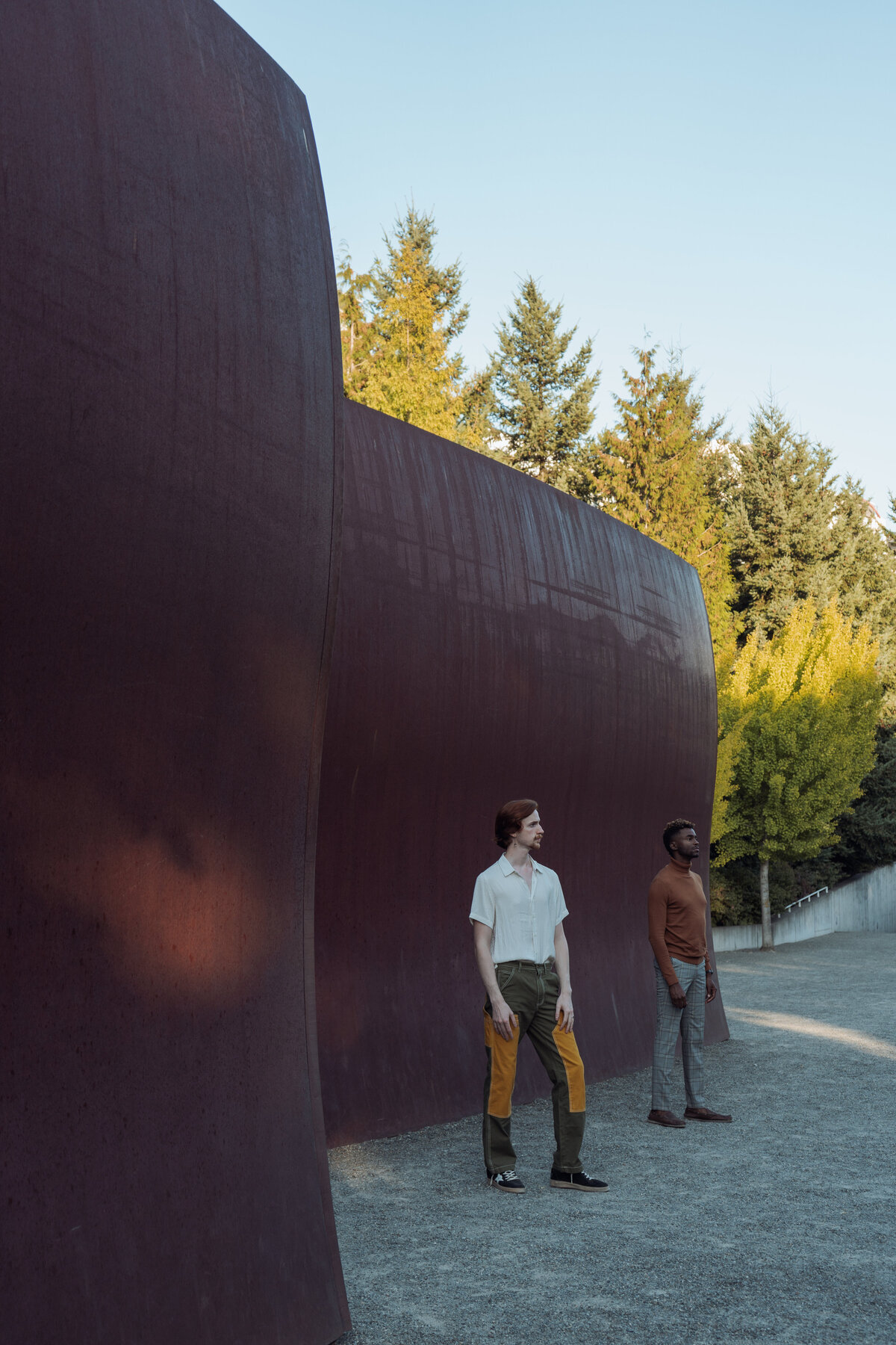Queer engaged couple at Olympic Park Sculpture in Seattle in an editorial pose looking off into the sunset