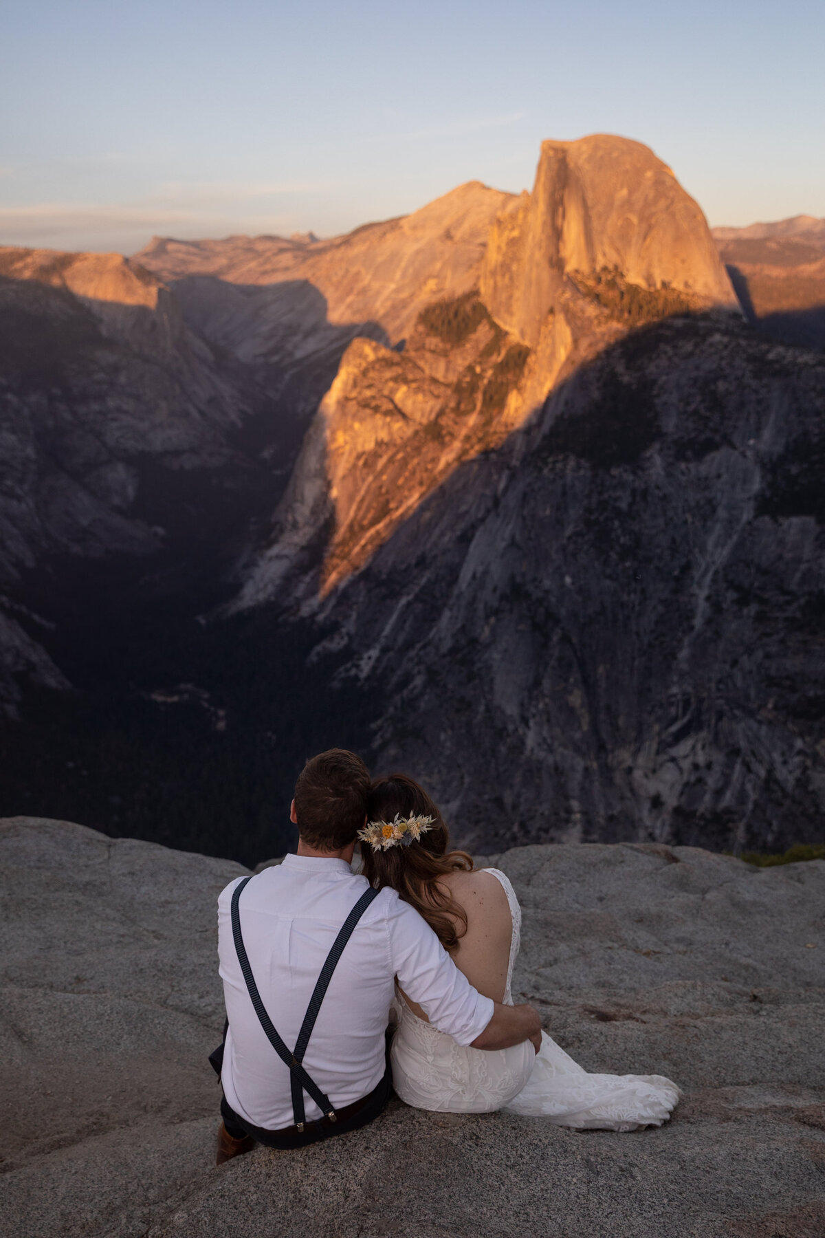 A bride and groom sit watching the sunset over Half Dome on their California elopement day.