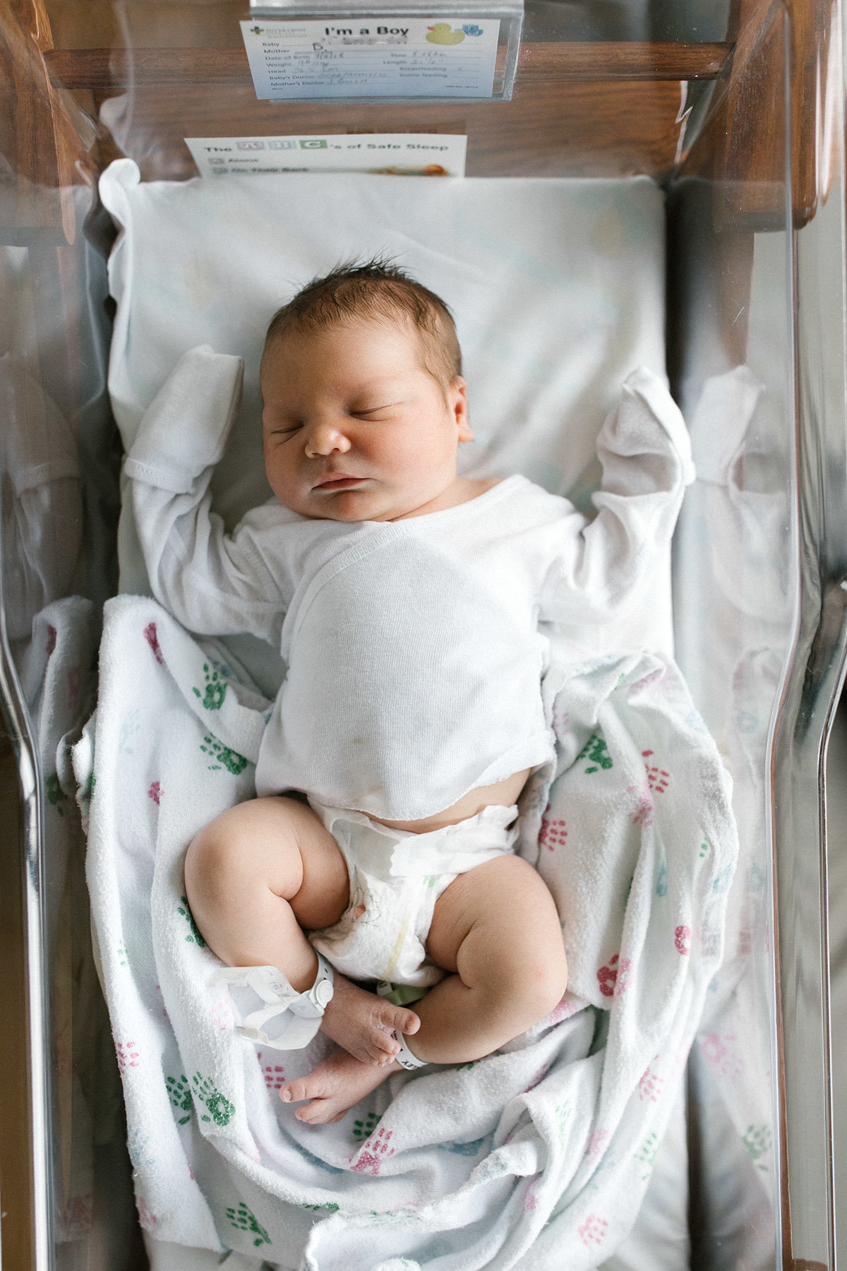 Newborn baby in the hospital laying on white hospital blanket by Elle Baker Photography