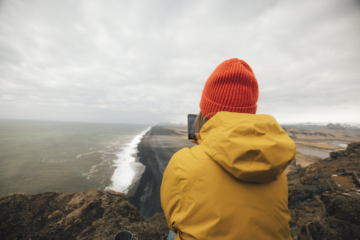 This is me in Iceland wearing a vibrant yellow jacket and orange hat enjoying the scenery and capturing the magic of intimate elopements