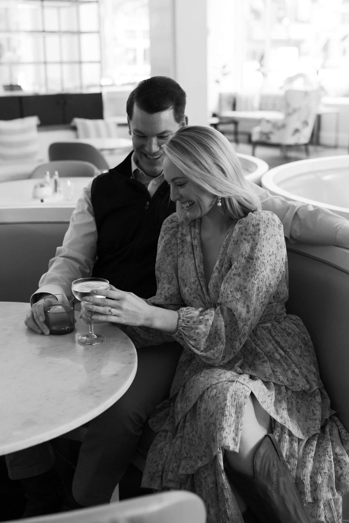 Quirk Hotel Richmond Restaurant Engagement Photos | black and white image of a couple sitting in the Quirk Hotel Restaurant having a cocktail and laughing