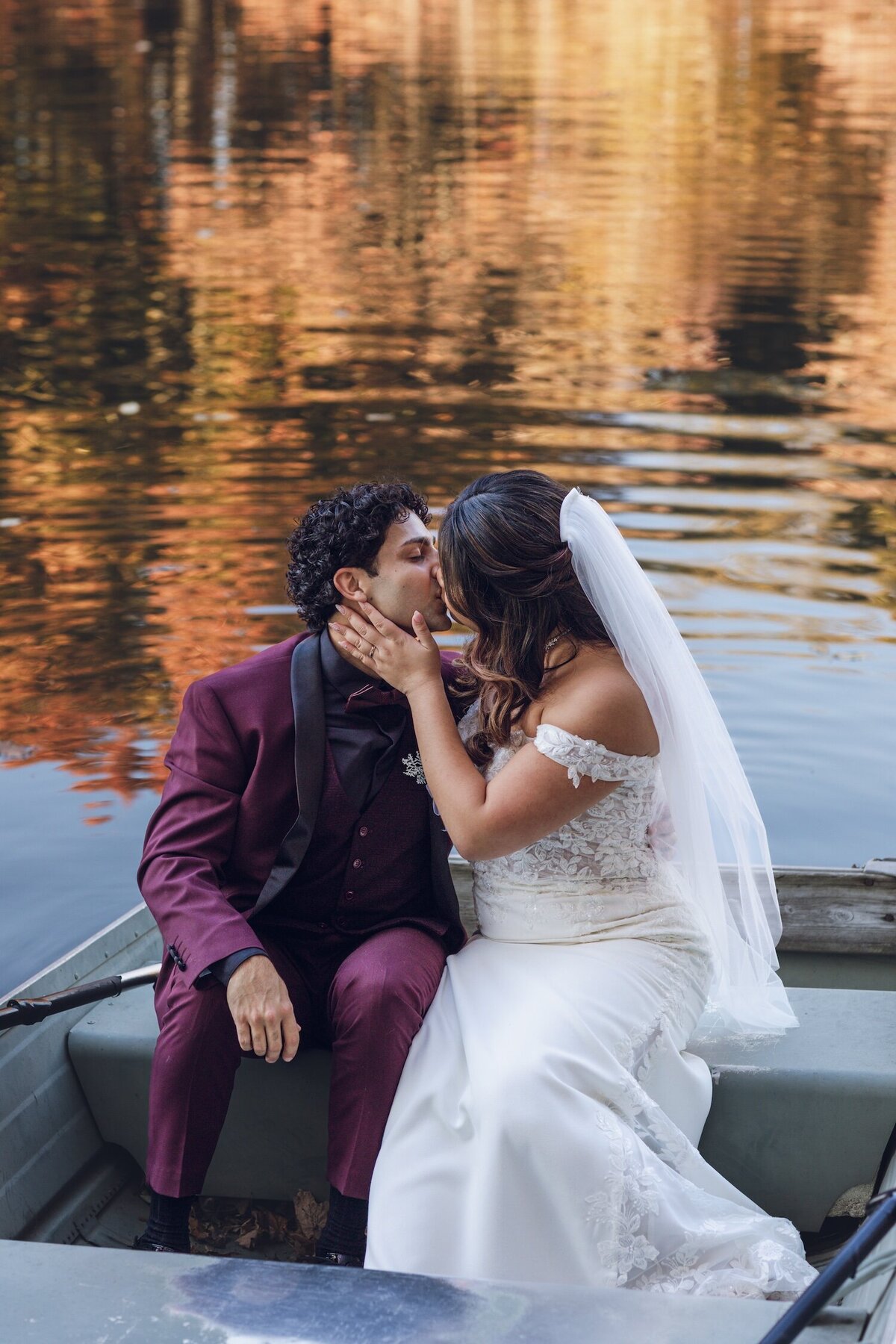 Groom leaning in to kiss the bride as they sit together in the rowboat.