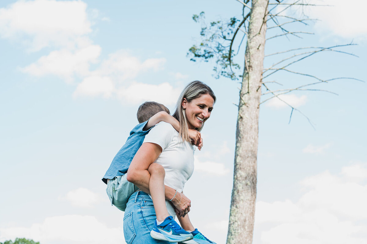 Smiling mother carrying her young child on her back outdoors, captured in a candid documentary family session