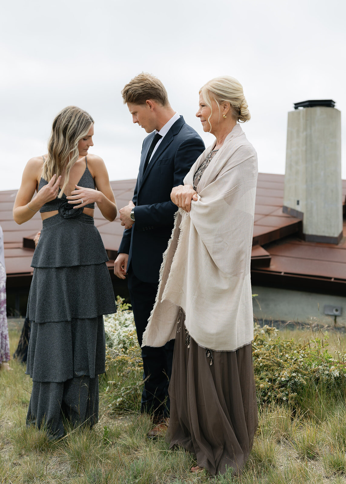 Three guests in formal attire chatting near a modern house