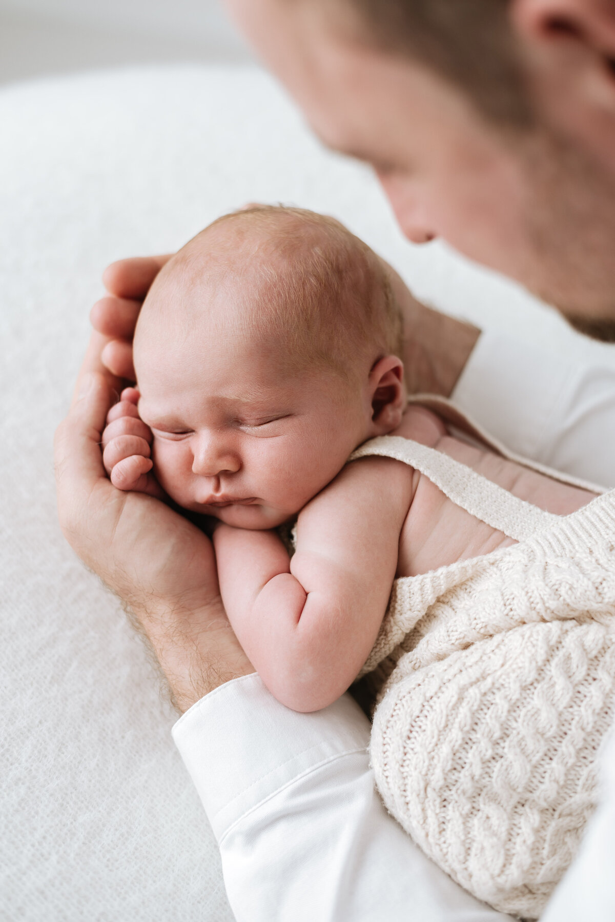 Father holding newborn baby boy in his hands and looking over him at newborn photoshoot in billingshurst