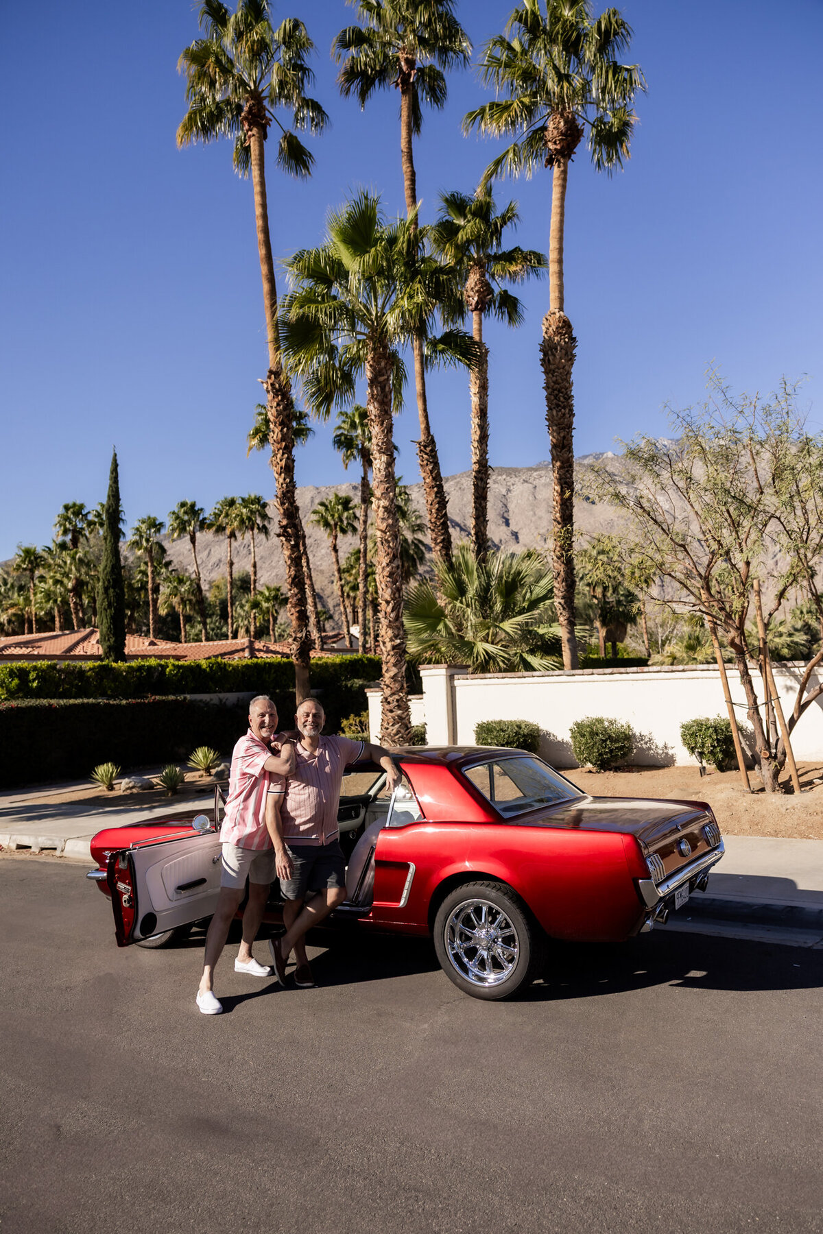 Couple driving a red convertible through Palm Springs, palms and pastel architecture lining the streets.