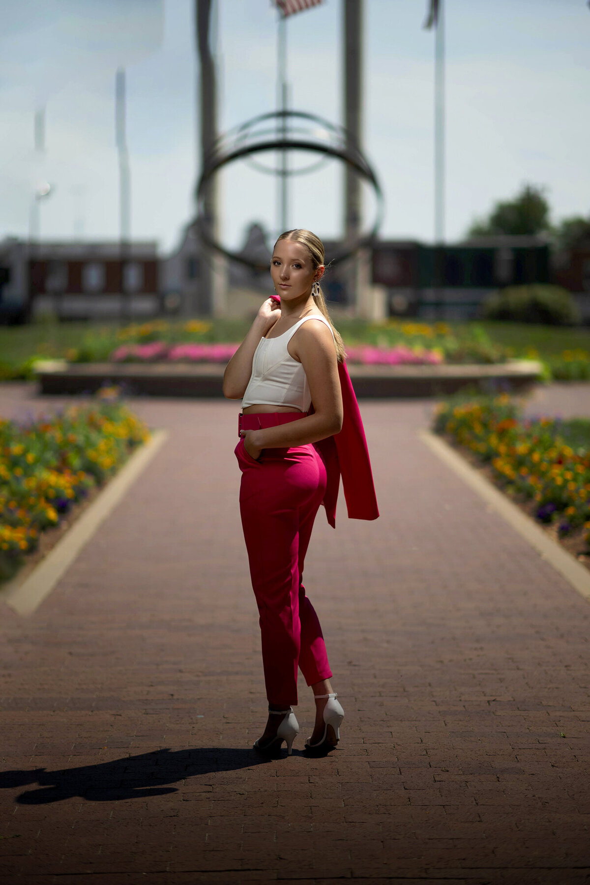 An image from a Pella Senior Photographer of a woman walking in a garden looking over her shoulder in a pink suit