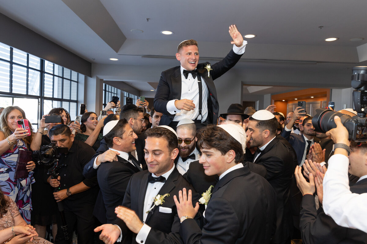 A groom behind held up by wedding guests