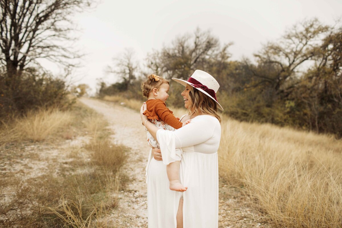 A tender maternity photo of the expectant mom in a white maternity dress, holding her daughter close to her while lovingly cradling her belly, captured by Chunky Monkey Photography.