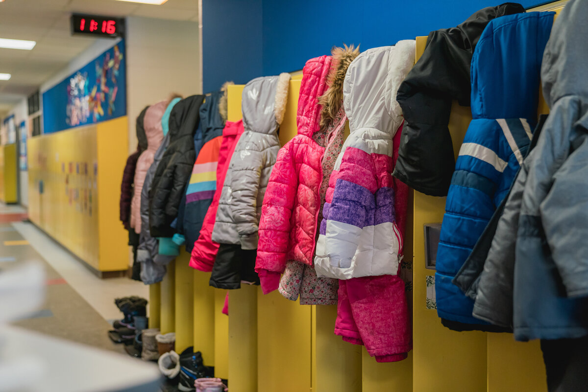 Children's winter coats hanging on yellow lockers in a school hallway
