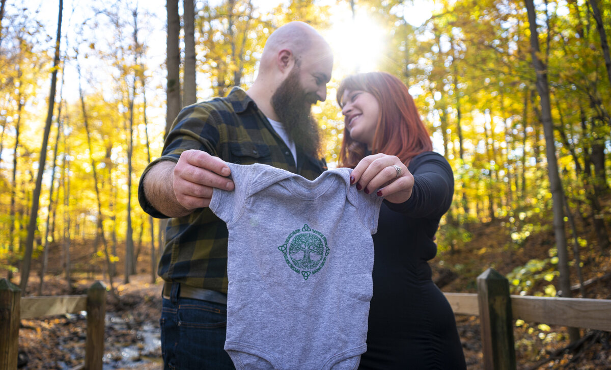 Bright portrait of new parents holding their baby's outfit outdoors