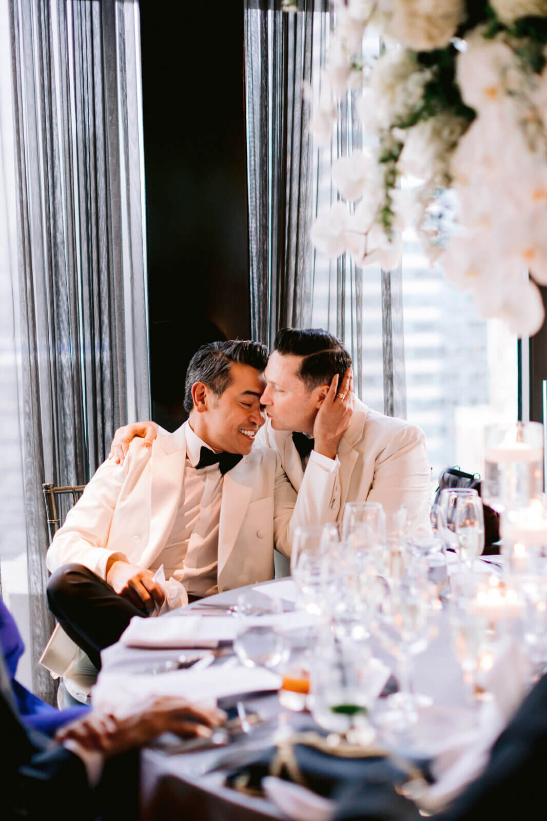 The groom is kissing the other groom on the nose during the reception in The Skylark, New York. Wedding Image by Jenny Fu Studio