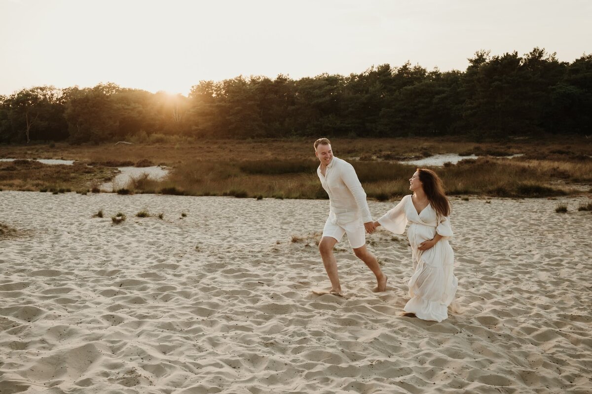 zwanger stel rennend in duinen met zonsondergang door fotograaf Eline Hemelt