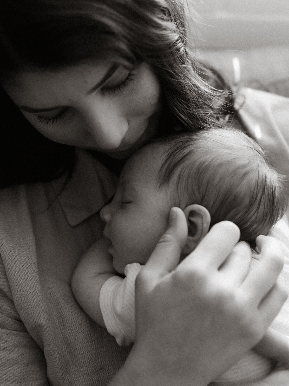 Newborn baby tenderly sleeping on mom's chest while sitting in the nursery, captioned in black and white.