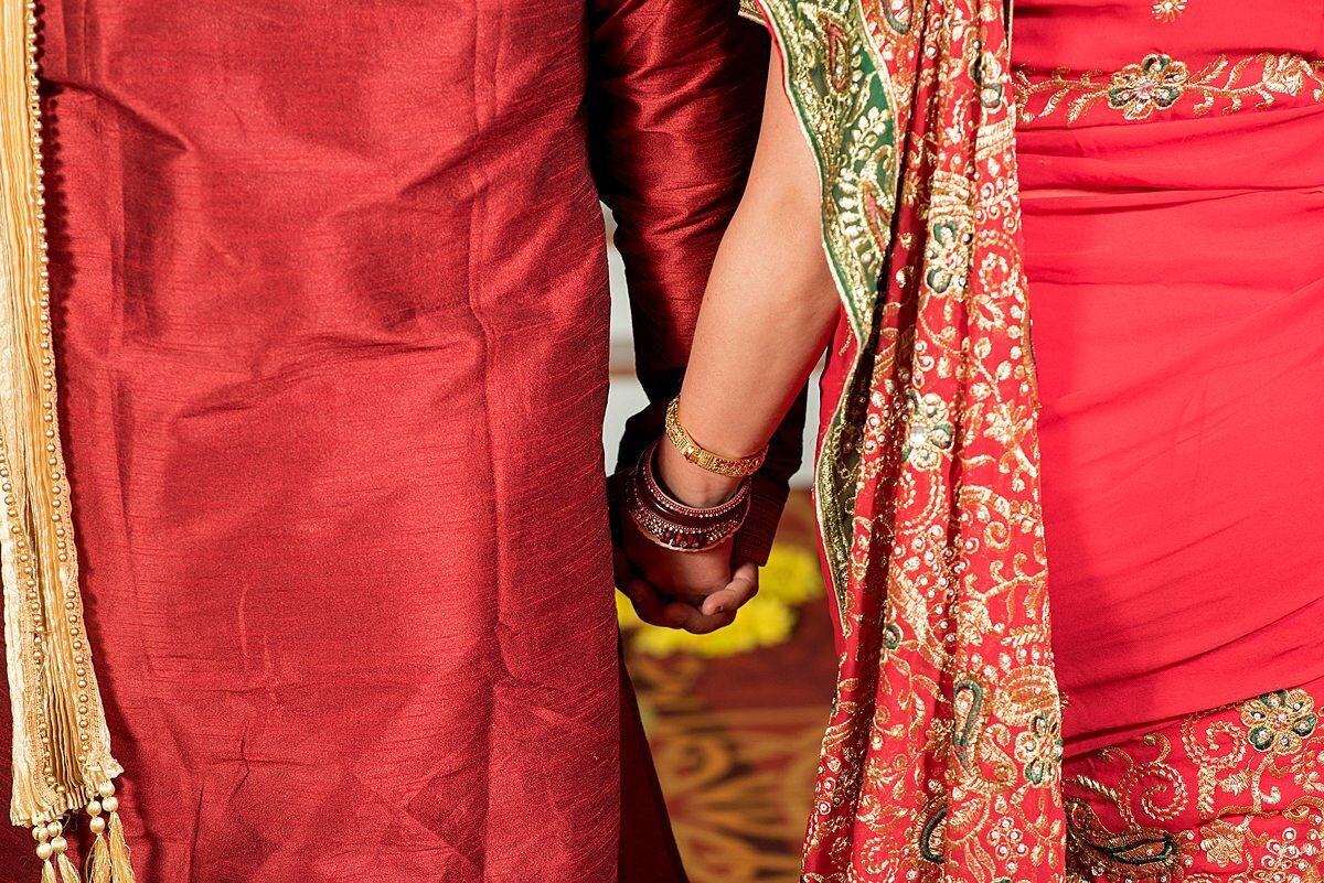 Indian Groom wearing a red and gold sherwani  holding hands with an Indian Bride wearing a gold, red and green saree at Indian wedding in Nashville, TN