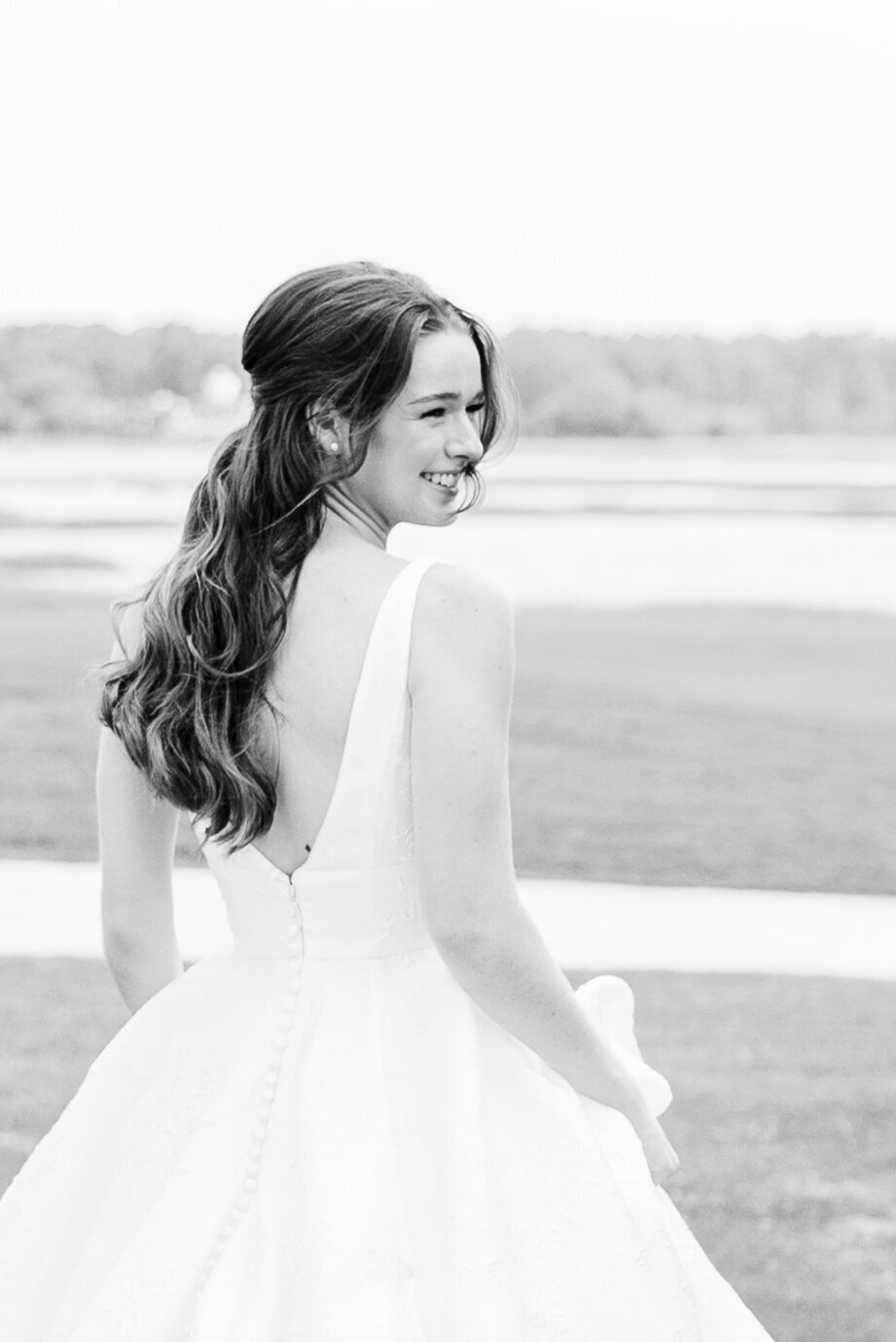 A radiant bride in a classic white gown smiles as she looks over her shoulder at her waterfront wedding at Dataw Island Club. A timeless black-and-white wedding portrait captured by Wedding Photographer charleston, SC.