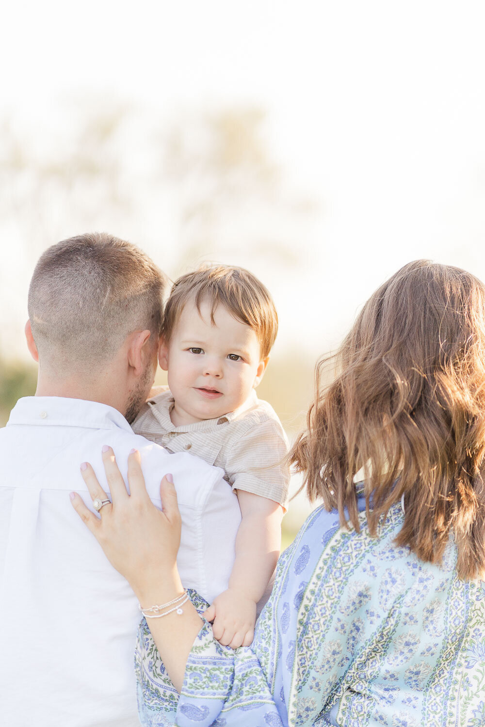 toddler peeking over parents' shoulders during spring mini session in South Riding, VA