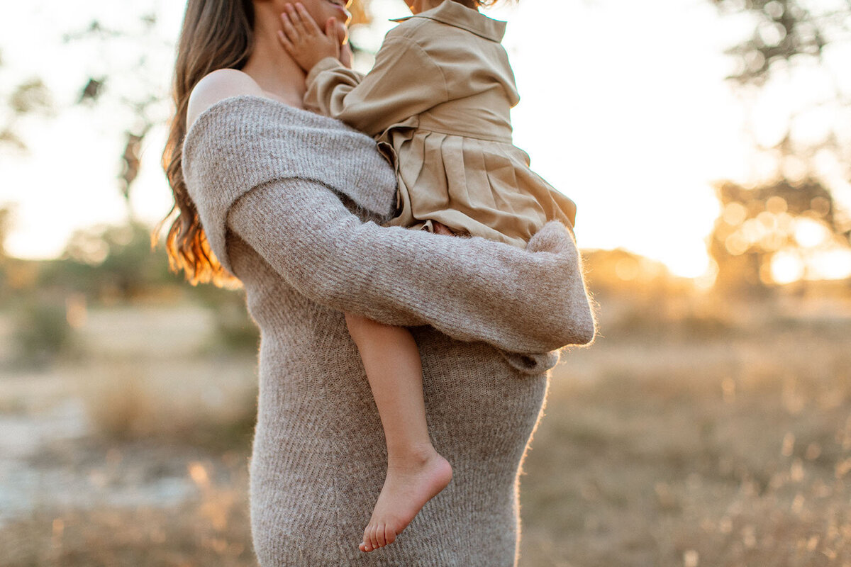 Expectant mother holding child outdoors in lovely natural light - Sara James creates meaningful maternity portraits featuring mom-to-be with sibling in beautiful San Antonio Texas outdoor locations