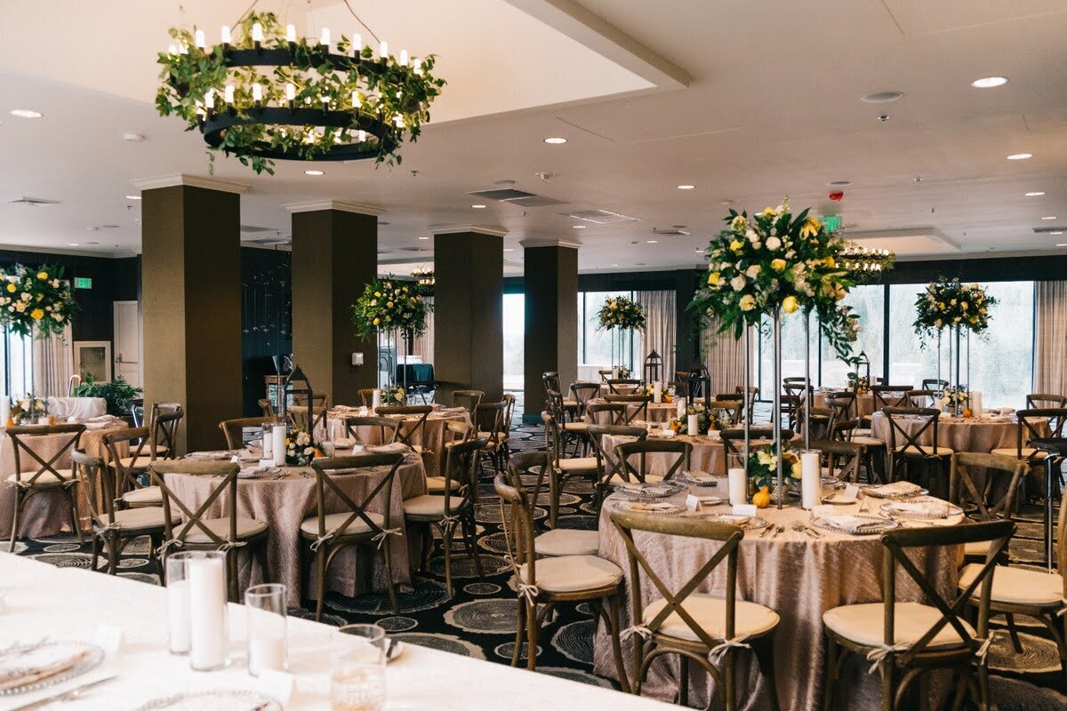 Indoor wedding reception featuring greenery-draped chandeliers and large floral arrangements.