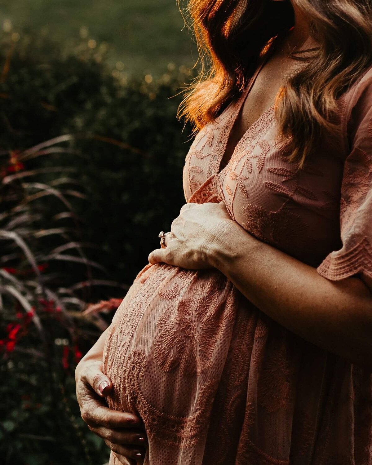 A pregnant woman in a pink dress, captured beautifully by a Pittsburgh maternity photographer in a field.
