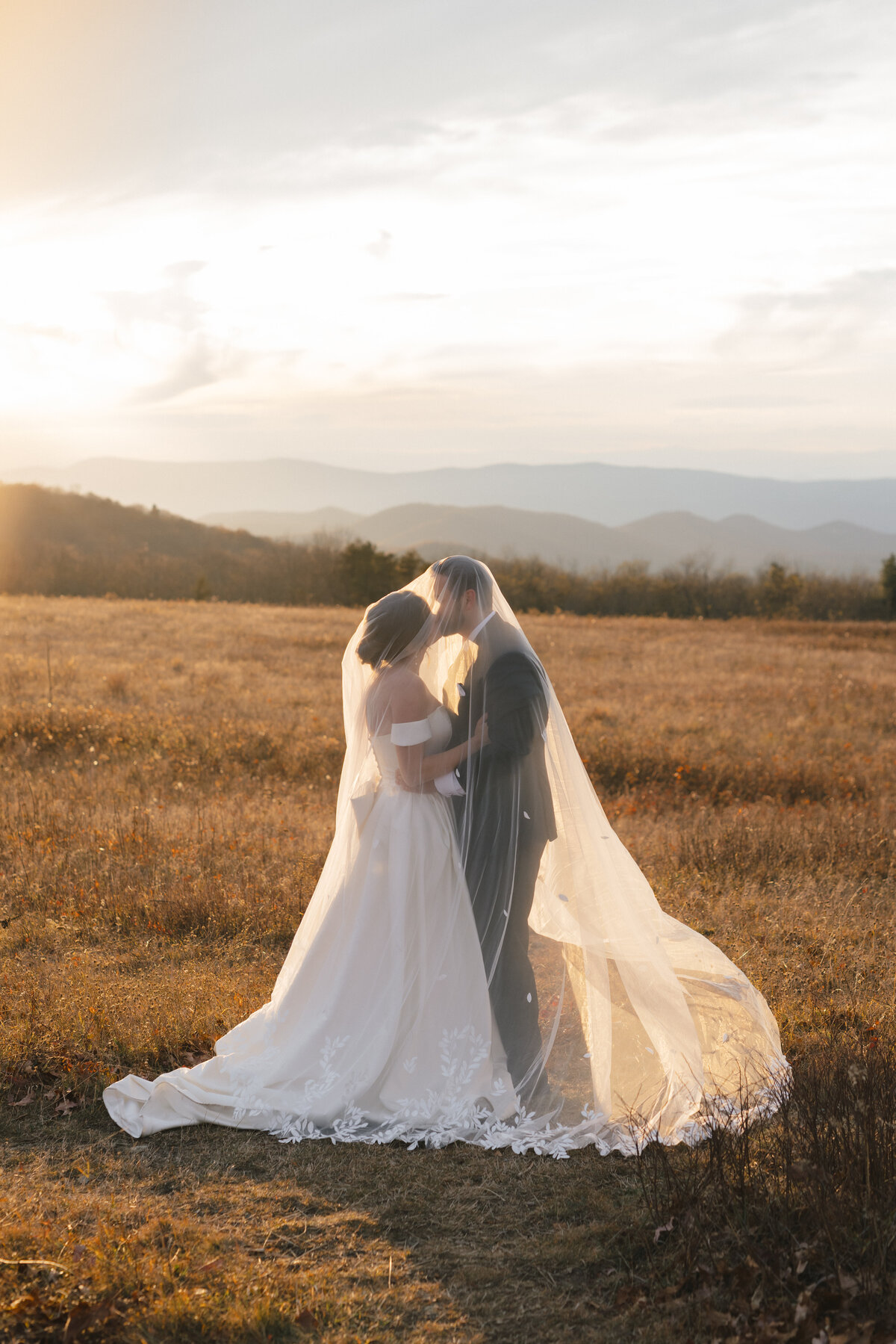Bride and groom embracing under the veil at sunset in a Blue Ridge mountain field, captured by a documentary-style Virginia wedding photographer.